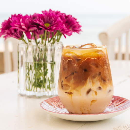 Iced caramel macchiato sitting on a table in front of a vase of bright flowers