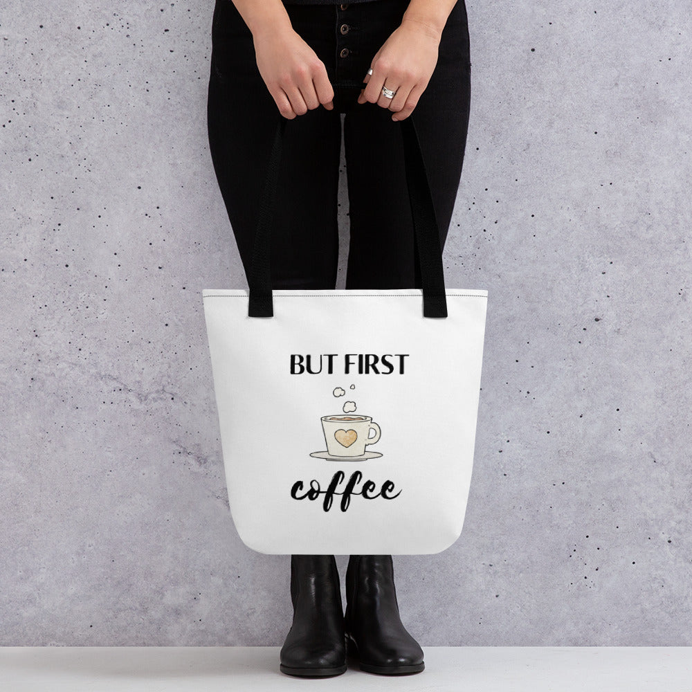 Woman holding a But First Coffee tote bag with a black handle.