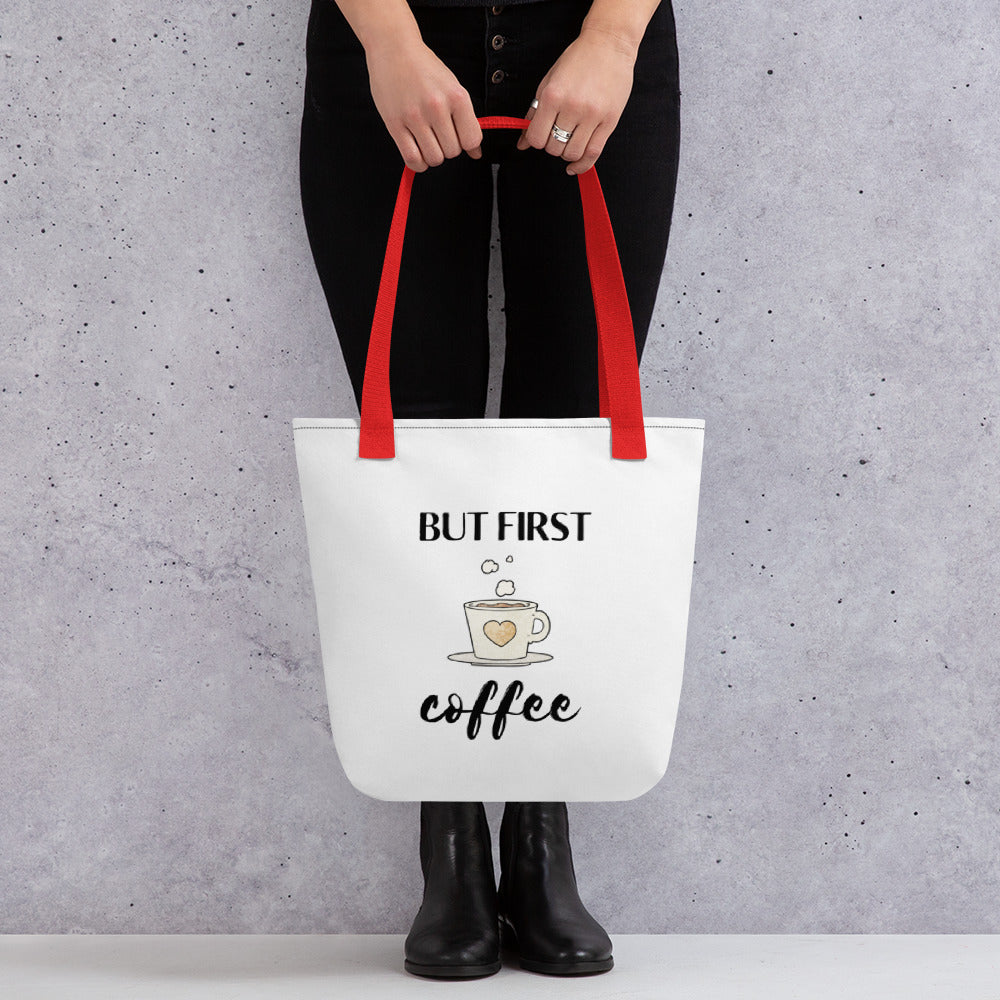 Woman holding a But First Coffee tote bag with a red handle.