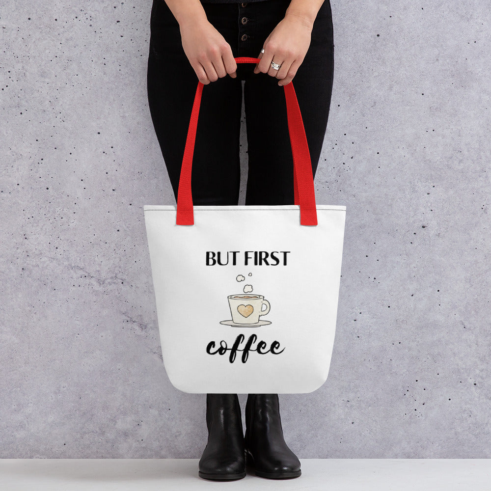 Woman holding a But First Coffee tote bag with a red handle.