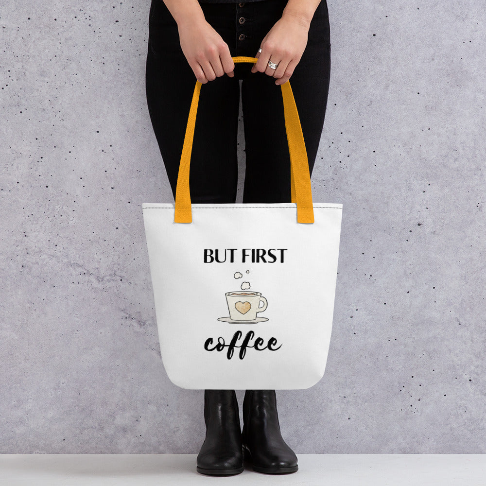 Woman holding a But First Coffee tote bag with a yellow handle.