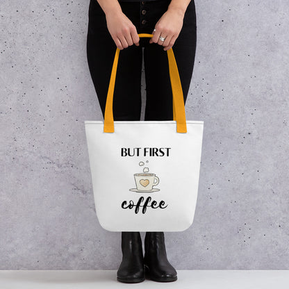 Woman holding a But First Coffee tote bag with a yellow handle.