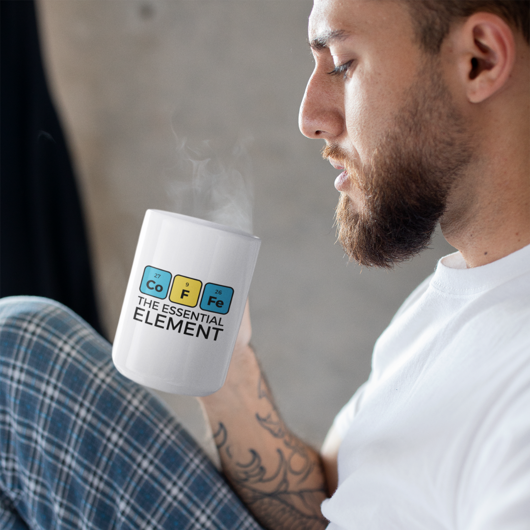man in his pajamas holding a steaming cup of coffee with Coffee The Essential Element written on it