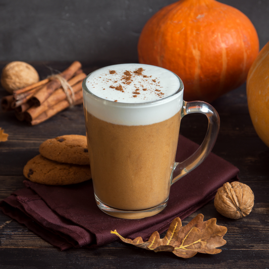 Glass mug of pumpkin spice latte surrounded by pumpkins, cinnamon sticks and spice cookies.