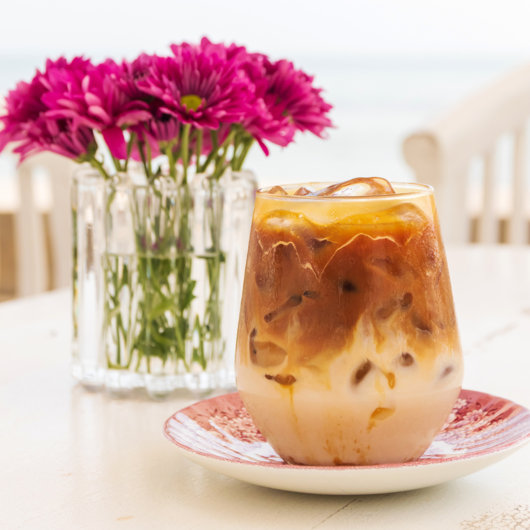 Iced caramel macchiato sitting on a table in front of a vase of bright flowers