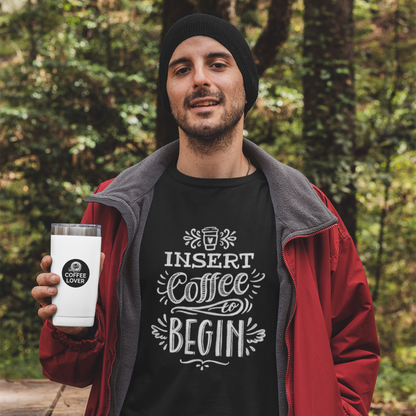 Man outdoors in nature holding a coffee travel mug wearing a black t-shirt that says Insert Coffee to Begin
