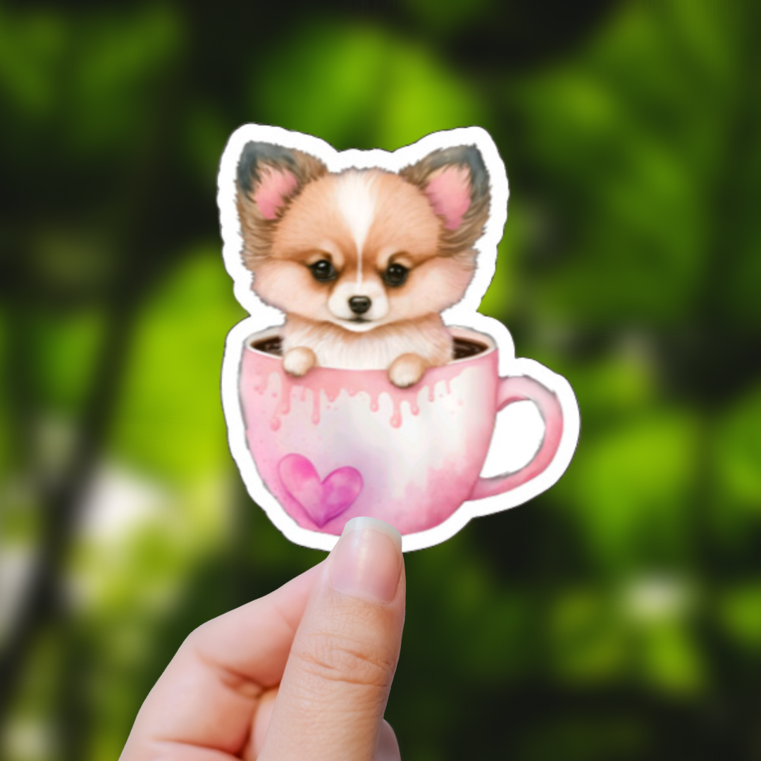 Sticker of a Corgi puppy sitting in a pink coffee mug with a heart. Done in watercolor. Background is blurred.