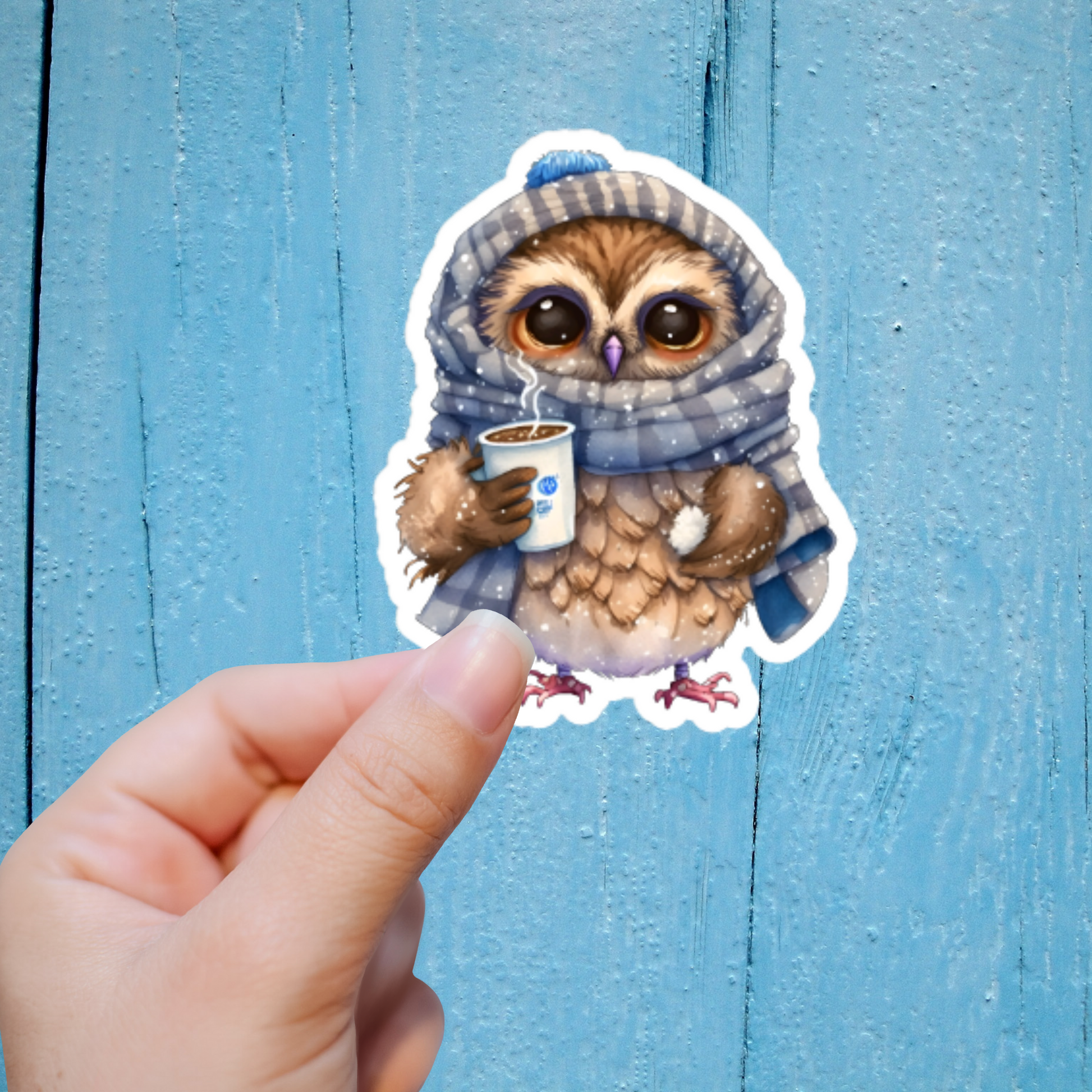Hand holding a sticker of a Chibi style owl wearing a winter hat and scarf holding a hot coffee